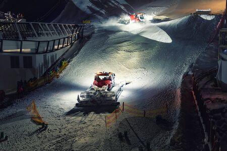 Two snowcat ratrack machines making night show performance on snow pister hill at alpine skiing resort Ischgl in Austria.の写真素材