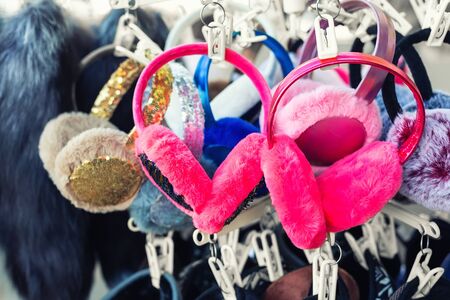 Lot of many multicolored bright fluffy fur earphones hanged on rack at store display for sale. Cute warm cold season clothes accessories.の写真素材