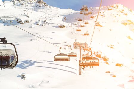 Ski lift ropeway on hilghland alpine mountain winter resort on bright sunny day. Ski chairlift cable way with people enjoy skiing and snowboardingの写真素材