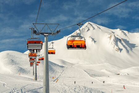 Ski lift ropeway on hilghland alpine mountain winter resort on bright sunny day. Ski chairlift cable way with people enjoy skiing and snowboarding.Banner panoramic wide view of downhill slopesの写真素材
