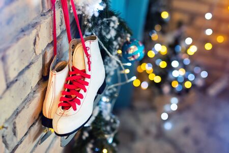 Pair of white vintage leather skates with red laces hanging on old rustic brick wall with blurred...
