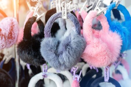 Lot of many multicolored bright fluffy warm winter fur earphones and gloves hanged on rack at store...