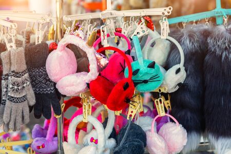 Lot of many multicolored bright fluffy warm winter fur earphones and gloves hanged on rack at store display for sale. Cute cold season clothes accessories.の写真素材