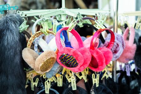 Lot of many multicolored bright fluffy warm winter fur earphones and gloves hanged on rack at store...
