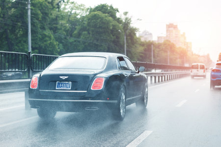 Kyiv, Ukraine - May 25th, 2019:Wet highway after heavy rain with warm sunset evening sun on background. Bentley vehicle riding high speed by rainy city street road. aquaplaning or hydroplaning effectのeditorial素材