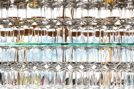 Wall of many empty transparent wine glasses on glass shelf at bar cafe or restaurant against backlit...