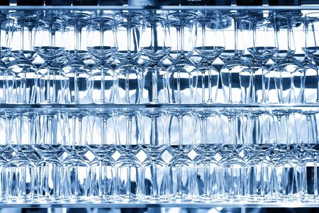 Wall of many empty transparent wine glasses on glass shelf at bar cafe restaurant against backlit...