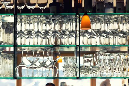 Wall of many empty transparent wine glasses on glass shelf at bar cafe or restaurant against backlit...