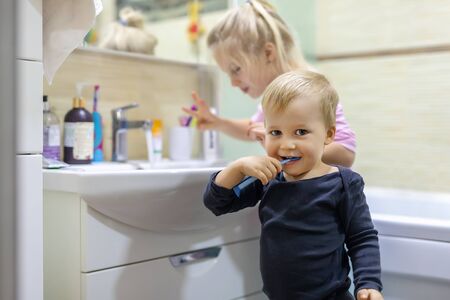 Two cute adorable blond caucasian siblings washing face and cleaning tooth with toothbrush at bathroom at home in morning. Little children brother and sister do daily higyene health care. Funny kidsの写真素材
