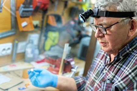Senior craftsman portrait with headlamp led torch working in workhop with tools and equipment on...