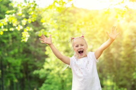 Cute adorable little caucasian child girl enjoy standing in forest during walk at summer day outdoor. Small happy kid at camping trip by nature parkland. Dreaming and feel free. Freedom lifestyle.の写真素材