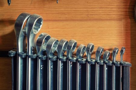 Set of used metal steel ring wrench organized and hanged in plastic holder against wooden wall....