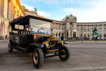 Vienna, Austria - January 12th, 2020: Sightseeing electric car styled vintage retro vehicle for tourist city tour against Vienna hofburg palace with blue sky on background. travel and tourism concept.のeditorial素材
