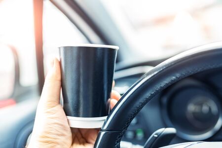 Close-up person hand holding black blank mockup paper cup woth hot coffee or tea takeaway drink...