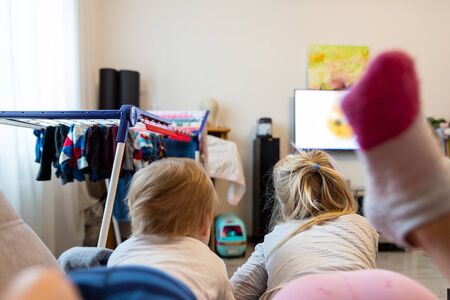 Back view of two cute little caucasian little boy and girl lying on sofa watching cartoons or movie on tv set with streaming service. Children stay home quarantine coronavirus outbreak spread danger.の写真素材