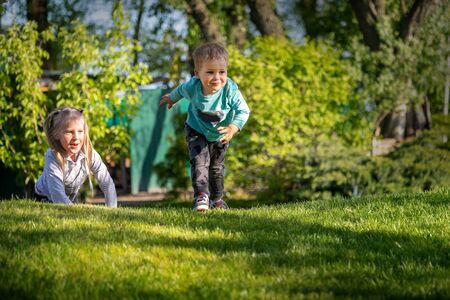 Two cute adorable playful caucasian blond children siblings little boy girl enjoy having fun playing together at home backtard green grass lawn at summer day. Brother sister happy childhood conceptの写真素材