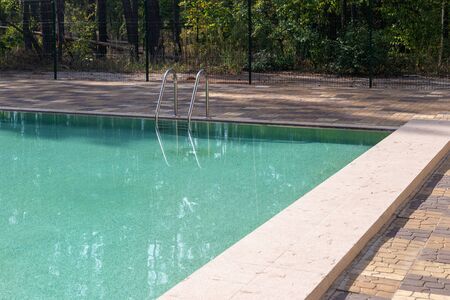 Big luxury empty rectangular swimming pool with clean blue water and ladder at tropical forest beach...