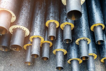 Heap of many new black insulated steel pipes at municipal construction site outdoors. Heating main...
