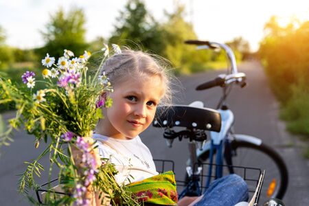 Portrait cute adorable caucasian blond little girl enjoy having leisure fun riding bicycle with family holding wild field flower at scenic rural country road on bright sunny day. Countryside vacationの写真素材