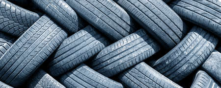 Old used weared car and truck wheels tyres pile stacked in rows stored for recycling. Heap of many rubber tires wall background. Idustrial pollution of environmentの写真素材