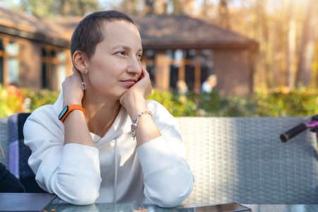 Young adult beautiful attractive stylish short haired woman enjoy sitting in street urban cafe, day-dreaming and looking with hope. Positive deep in thought girl portrait in autumn park outdoorsの写真素材