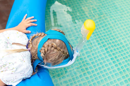 Cute adorable caucasian blond little girl making experiment try diving in pool with full face snorkel mask in inflatable pool at house yard. Stay home lockdown quarantine new normal. Travel conceptの写真素材