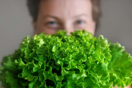 Young adult beautiful caucasian happy smiling woman portrait holding green fresh lettuce salad crop in front face. Healthy food and nutrition concept. Green oraganic eco bio natural vegan mealの写真素材
