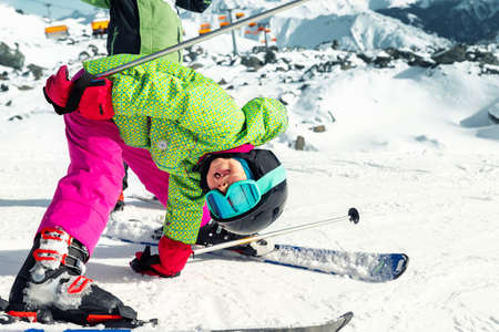 Active adorable preschooler caucasian kid girl portrait with ski in helmet, goggles and bright suit enjoy winter sport activities puh hand up. Little child having fun standing upside down on peak.の写真素材