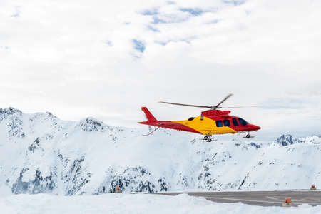 Mountain ski life rescue medic helicopter taking-off from station helipad to search injured skiers and help at accident. Emergency chopper at austrian alpine skiing resort. Alps landsapeの写真素材