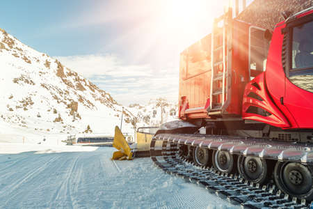 Red modern snowcat ratrack with snowplow snow grooming machine preparing ski slope piste hill at...