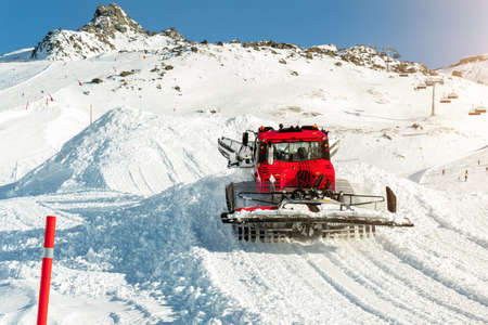 Red modern snowcat ratrack with snowplow snow grooming machine preparing ski slope piste hill at alpine skiing winter resort Ischgl in Austria. Heavy machinery mountain equipment track vehicle.の写真素材