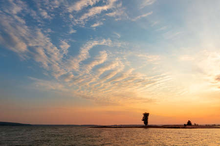 Dramatic colorful orange to blue sunset or sunrise sky landscape with lake or river bank and tree silhouette. Natural beautiful cloudscape dawn wallpaper.Ripple water reflection twilight panorama.の写真素材