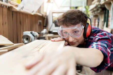 Young attractive 30-40 professional female carpenter looking grinding raw wood with sandpaper in...