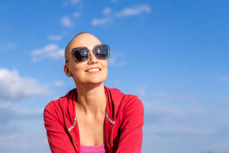Young adult beautiful happy attractive caucasian bald shaved woman portrait in sunglasses enjoy looking far away and smiling against blue sky background outdoors. Confident joyful female personの写真素材