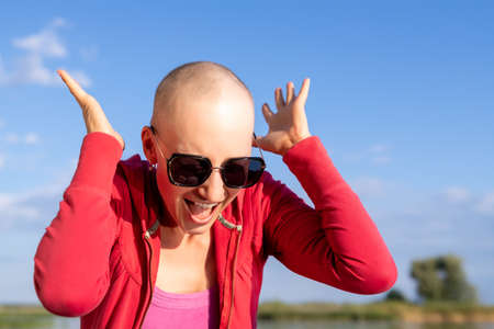 Portrait of young adult beautiful caucasian short haired bald woman in sunglasses shouting with hands raised up and annoyed screaming face expression. Unhappy stressed girl shouting in panic outdoorsの写真素材