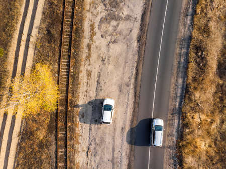 Aerial overhead top down bird eye drone view of asphlat rural country road with parked and driving...