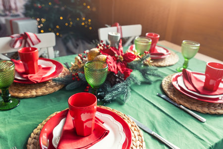 Beautiful festive holiday xmas family table setting served for 4 persons with light, christmas tree and many gifts on background. Simple warm rustic new year eve dinner decoration indoor homeの写真素材