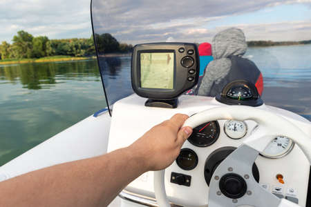 Young adult caucasian man POV enjoy having fun driving fast motorboat with family on pond water surface at sunset evening time. Male person sailing on speedboat with sonar and compass equipment toolsの写真素材