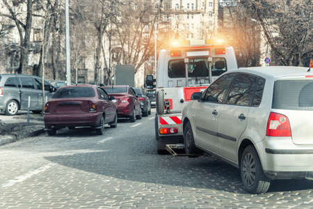 Car evacuation police service by tow truck machine on city downtown street center due parking traffic rules violation. Emergency road assistance service motorway. Automotive trailer carrier transportの写真素材