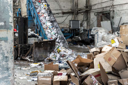 Shreding wastepaper mill conveyor belt for recycling paper wrap, garbage and cardboard against bales of used carton boxes collected for recycle and reuse at industrial plant or factory.Sustainableの写真素材