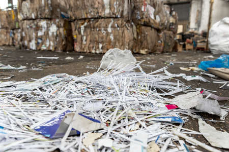 Dump pile of used shreded paper wrap and document against bales of compressed cardboard collected for recycling and reuse at industrial plant or factory. Sustainable materials and environment conceptの写真素材