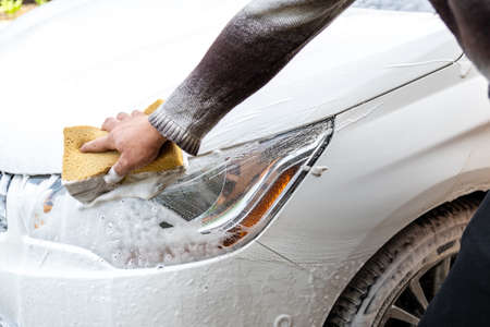 Close-up detail manual car wash with high pressure water equipment pump and soapy sponge at home...