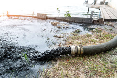 Close-up big pipe of power pump machine pouring mud sludge waste water with sand and silt on ground....