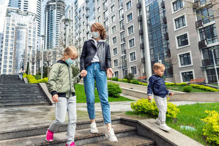 Young adult caucasian mother walking downstairs together with son and daughter children in city center downtown against building. New normal urban people lifestyle post virus lifeの写真素材