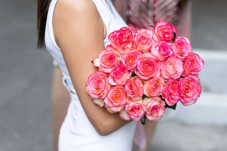 Closeup female person hand holding big bunch of fresh natural tender pink roses at date on city street outdoors. Happy young adult caucasian woman with beautiful bridal huge flower bouquet outsideの写真素材