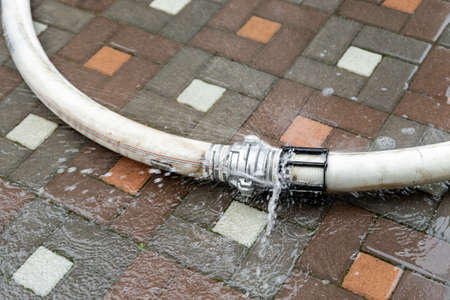 Close-up old worn out broken fire hose leaking with high pressure water waste during firefighter working on accident at city residential building. Water supply connection burstの写真素材