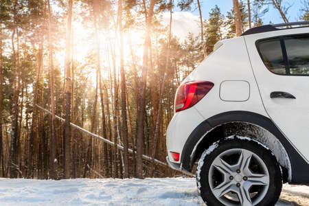 Back part of unknown small suv car parked at countryside dirt road in snowdrift near forest at...