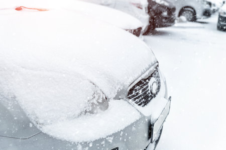 Cars parked in row at outdoor parking in winter. Vehicles covered by snow during heavy snowfall. Snowstorm or blizzard cold season weather forecast. Ice storm automobile park lot storage at morningの写真素材