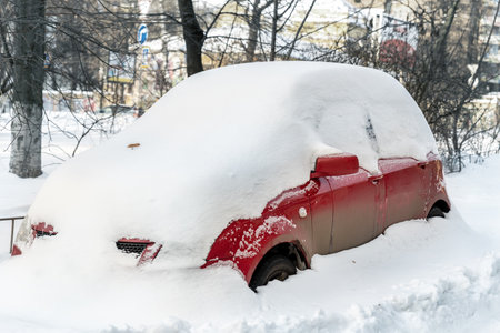 City street driveway parking lot spot with small car covered snow stuck trapped after heavy blizzard snowfall winter day by big snowy pile. Snowdrifts and freezed vehicles. Extreme weather conditionsの写真素材