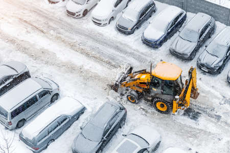 Tractor loader machine uploading dirty snow into dump truck. Cleaning city street, removing snow and ice after heavy snowfalls and blizzard. Snowplow outdoors clean pavement sidewalk road drivewayの写真素材